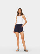 Woman wearing a white sleeveless top and navy shorts on a white background