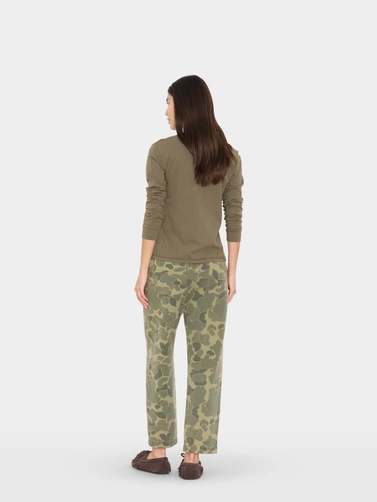 Woman wearing a green sweater and camouflage pants on a white background