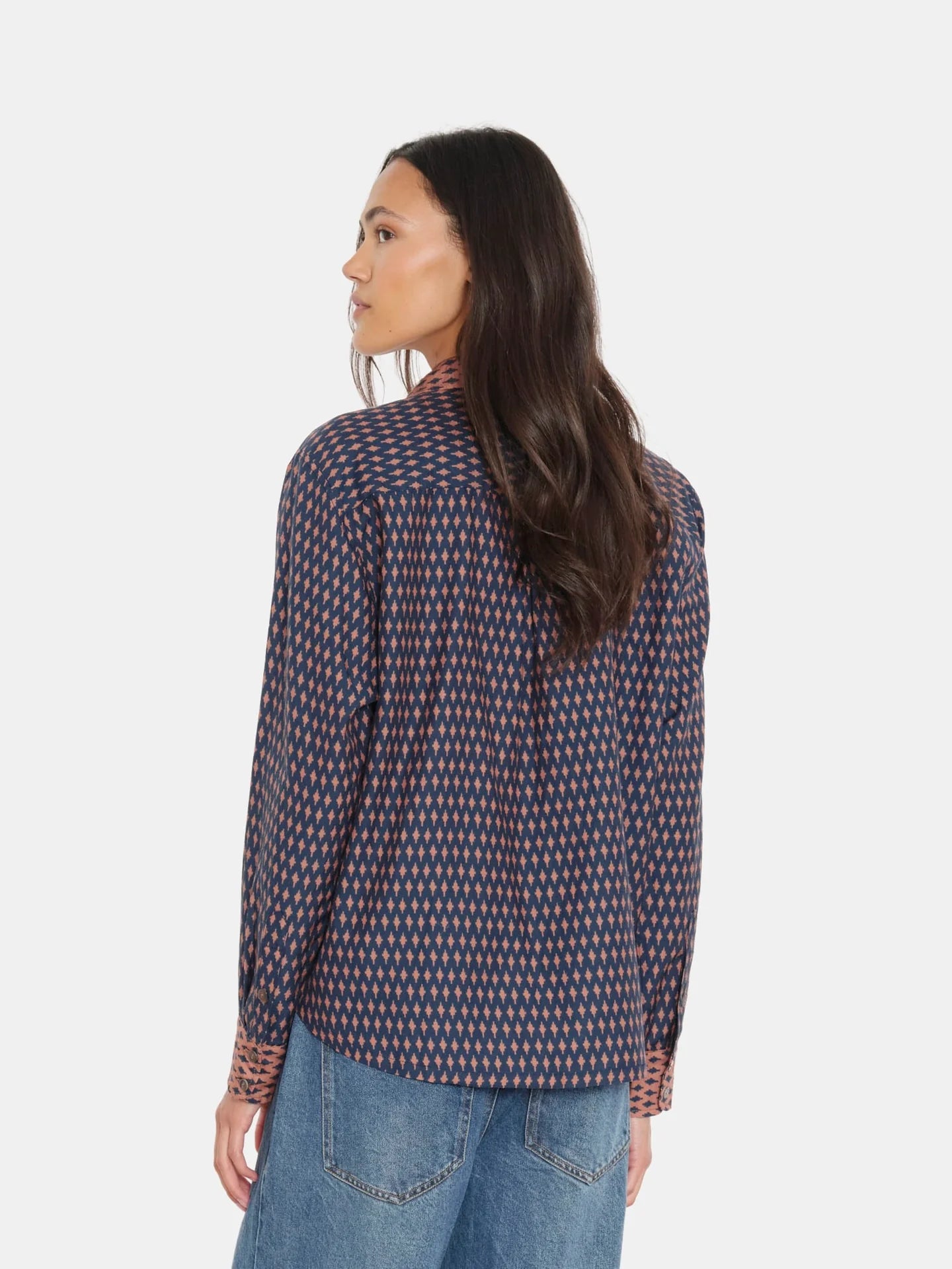Woman wearing a patterned shirt and jeans on a white background