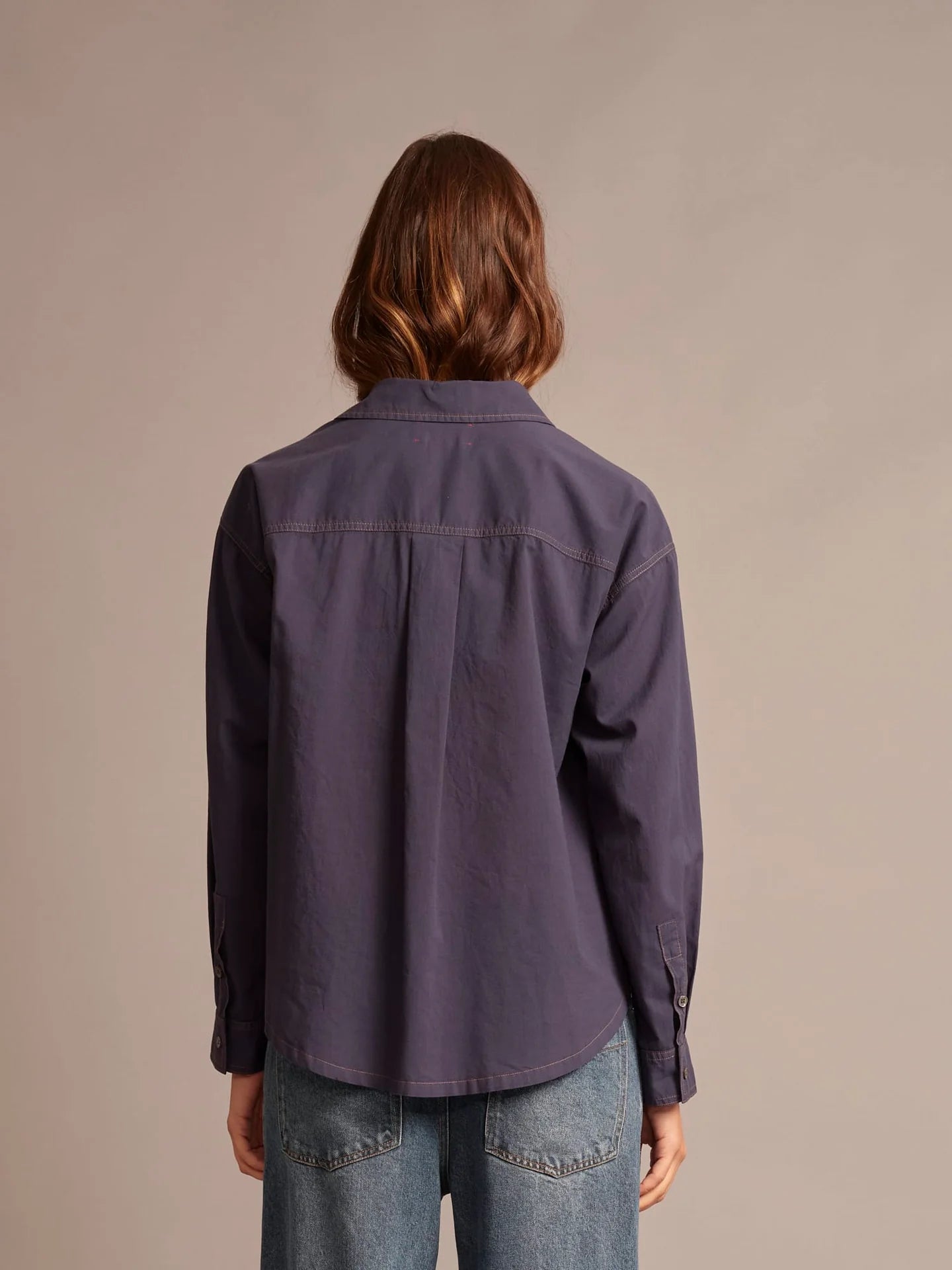 Person wearing a long-sleeve purple shirt against a beige background