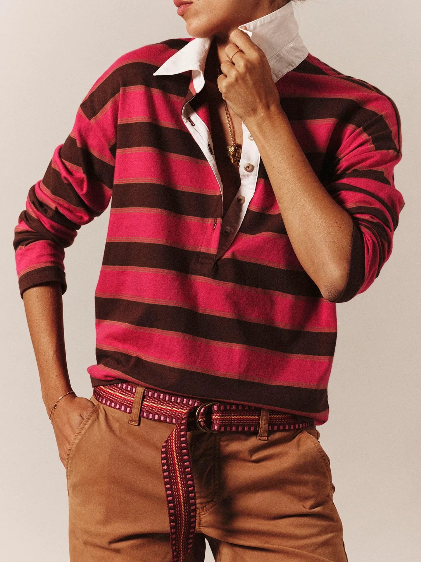 Person wearing a red and black striped shirt with a white collar, brown pants, and a patterned belt.
