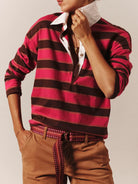 Person wearing a red and black striped shirt with a white collar, brown pants, and a patterned belt.