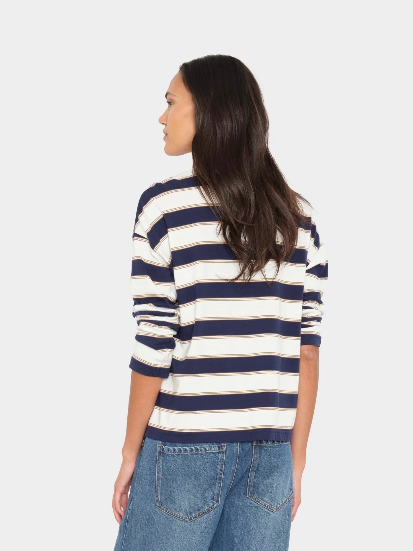 Woman wearing a navy and white striped sweater with blue jeans on a light gray background