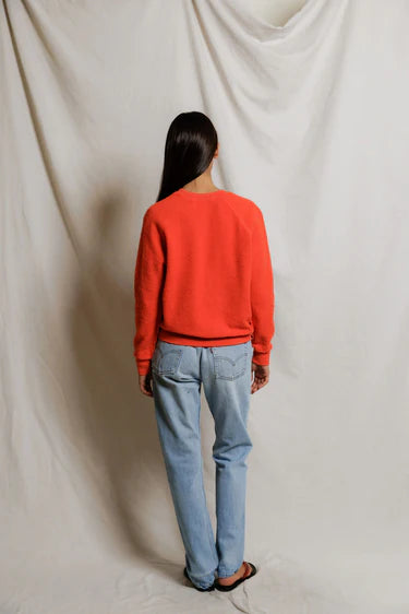 Person wearing a red sweater and blue jeans standing against a plain white background