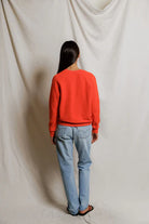 Person wearing a red sweater and blue jeans standing against a plain white background