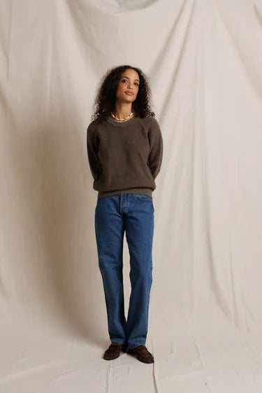 Person wearing a brown sweater and blue jeans against a plain background
