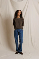 Person wearing a brown sweater and blue jeans against a plain background