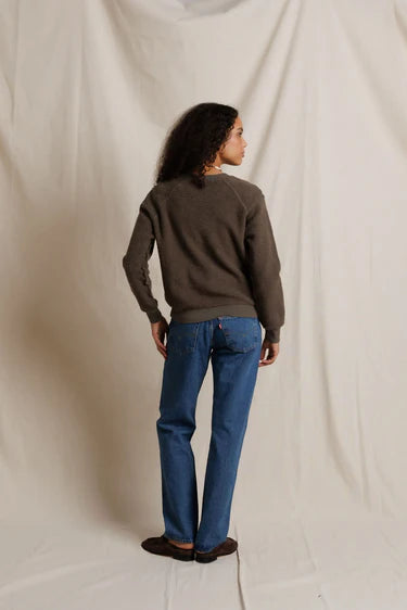 Person wearing a brown sweater and blue jeans against a plain background