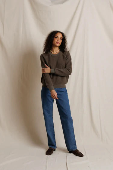 Woman wearing a brown sweater and blue jeans against a plain background