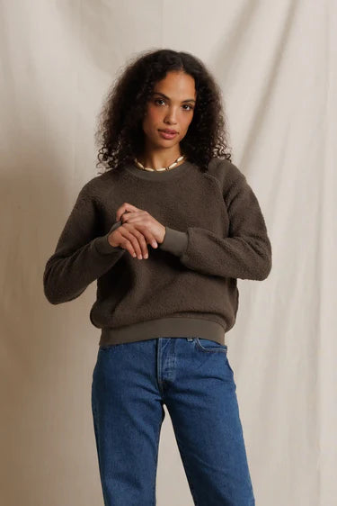 Woman wearing a brown sweater and blue jeans against a beige background