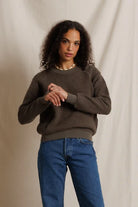 Woman wearing a brown sweater and blue jeans against a beige background