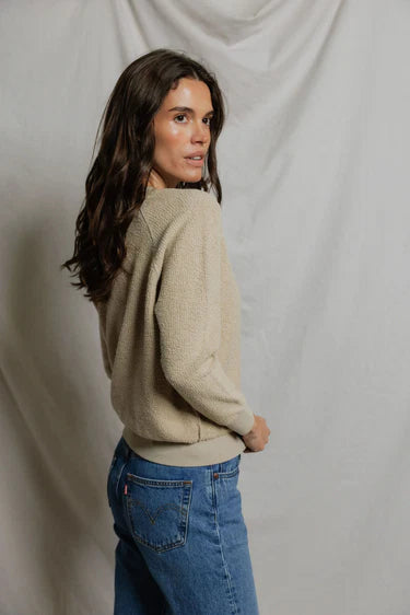 Woman wearing a beige sweater and blue jeans against a plain background