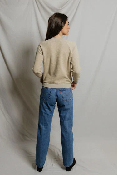 Person wearing a beige sweater and blue jeans against a plain background
