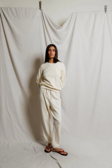 Woman wearing a white outfit standing against a plain white curtain.