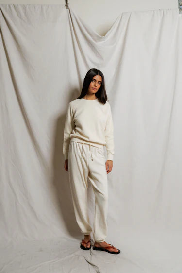 Woman wearing a white outfit standing against a plain white curtain