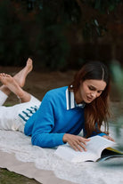 Woman in blue sweater reading a book outdoors on a blanket