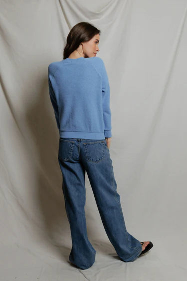 Person wearing a blue sweater and jeans against a plain background