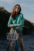 Woman in teal sweater with bicycle on beach