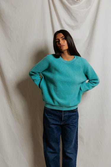 Woman wearing a teal sweater and blue jeans against a plain background
