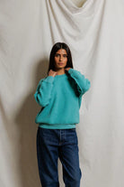 Person wearing a teal sweater and blue jeans against a plain background