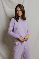 Woman wearing a purple sweater and pants against a plain background