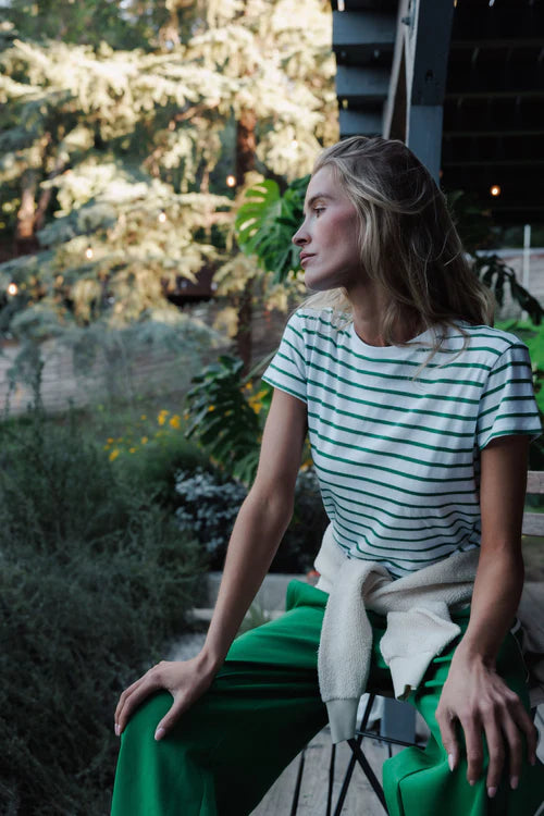 Woman sitting outdoors in a garden wearing a green and white striped shirt.