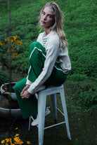 Woman in green pants and white sweater sitting on a stool outdoors.
